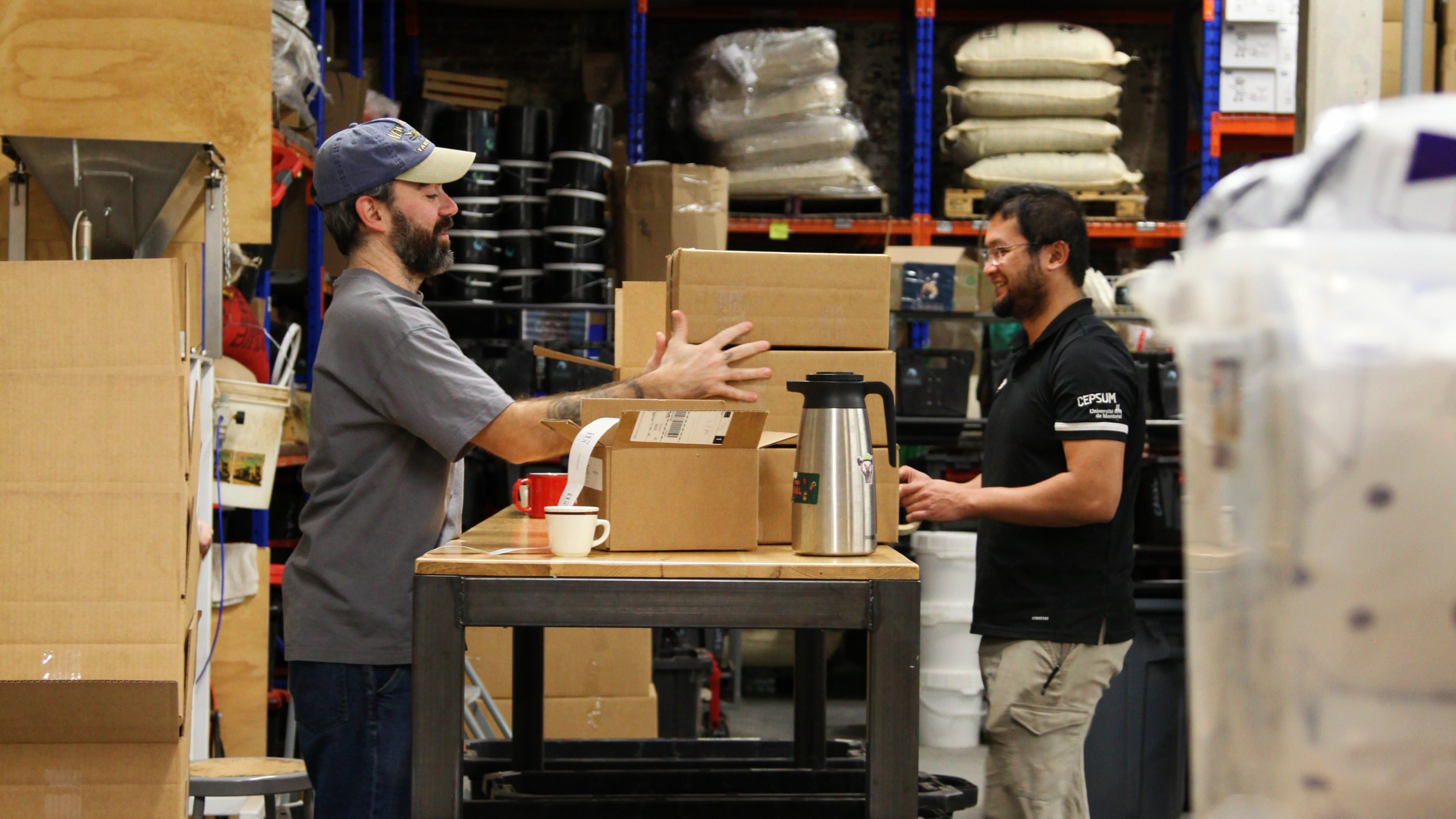 Two workers in a warehouse setting with boxes and packaging materials.